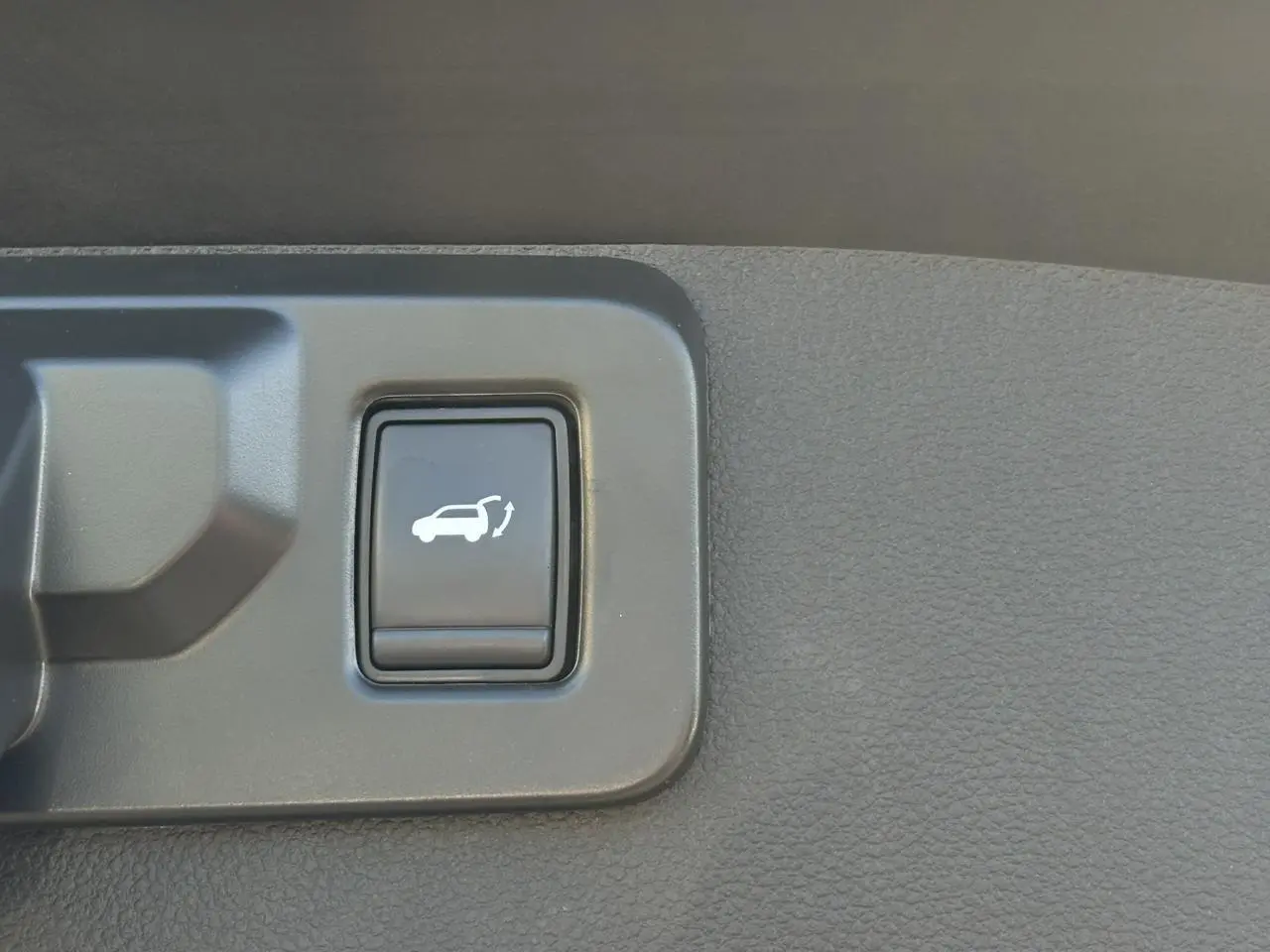 Gros plan sur le bouton d'ouverture du hayon mains libres dans l'habitacle d'une Renault Symbioz gris Cassiopée.
