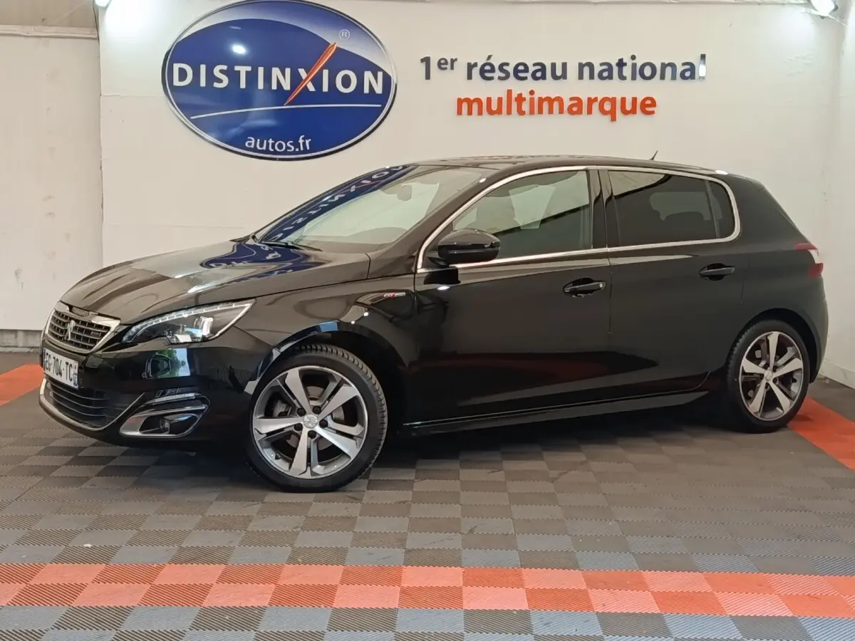 Vue latérale droite d'une Peugeot 308 noire GT Line 2016, avec jantes alliage et phares LED visibles en intérieur showroom.