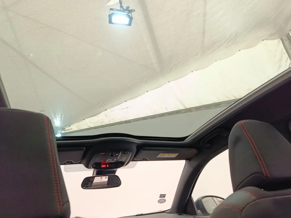 Vue intérieure du toit ouvrant panoramique et des appuis-tête noirs avec surpiqûres rouges d'une Peugeot 308 GT Line noire.