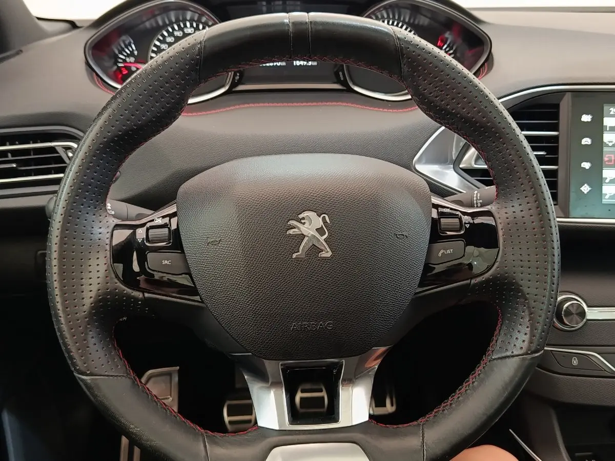 Vue rapprochée du volant cuir noir perforé avec surpiqûres rouges de la Peugeot 308 GT Line 2016, tableau de bord en arrière-plan.