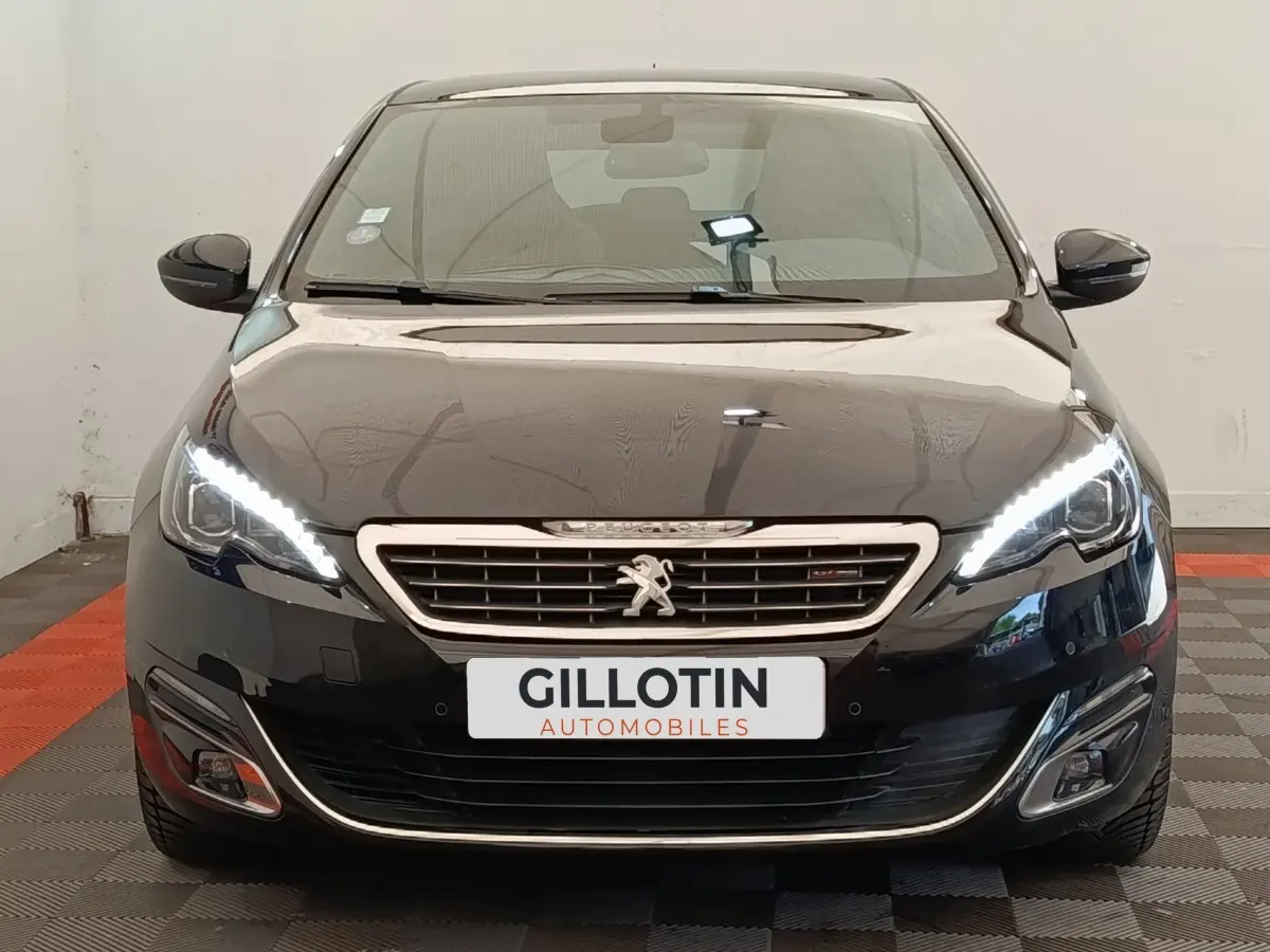 Vue frontale d'une Peugeot 308 noire avec feux LED allumés et calandre chromée distinctive.