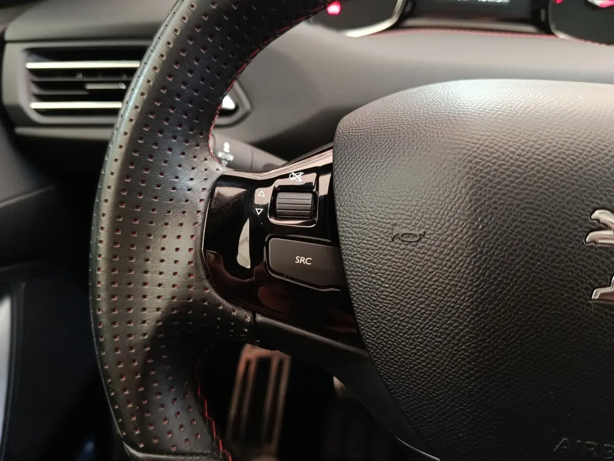 Gros plan sur le volant cuir perforé côté gauche du Peugeot 308 noir, avec commandes multimédia intégrées.