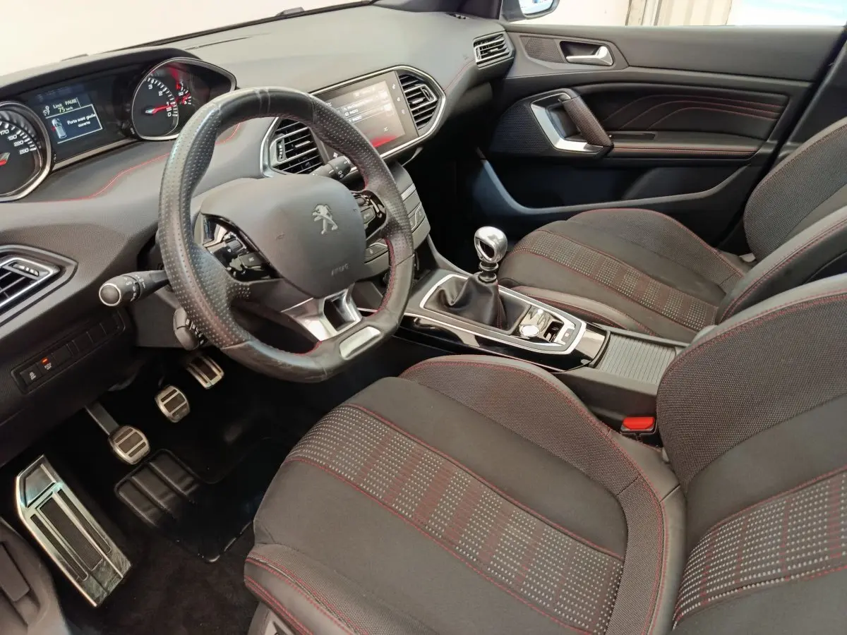 Intérieur Peugeot 308 GT Line 2016 vu côté conducteur, volant cuir, sièges tissu noirs avec surpiqûres rouges.