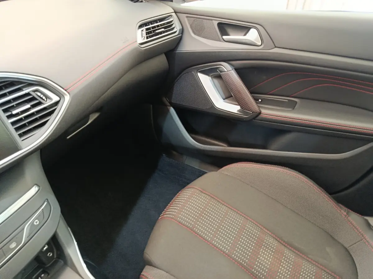 Vue intérieure côté passager avant de la Peugeot 308 GT Line 2016, sièges noirs avec surpiqûres rouges et détails de la portière.