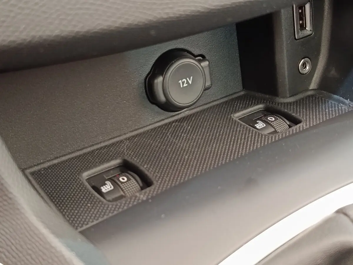 Gros plan sur la console centrale noire de la Peugeot 308, montrant la prise 12V et les commandes de sièges chauffants.