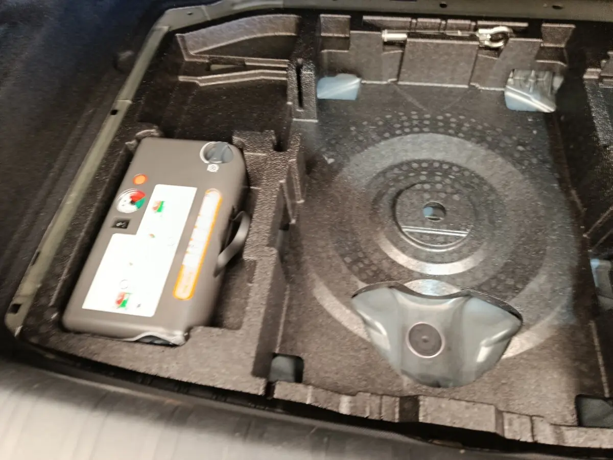 Vue rapprochée du coffre de la Peugeot 308 noir, montrant le rangement sous la tablette avec compresseur et espace pour roue de secours.