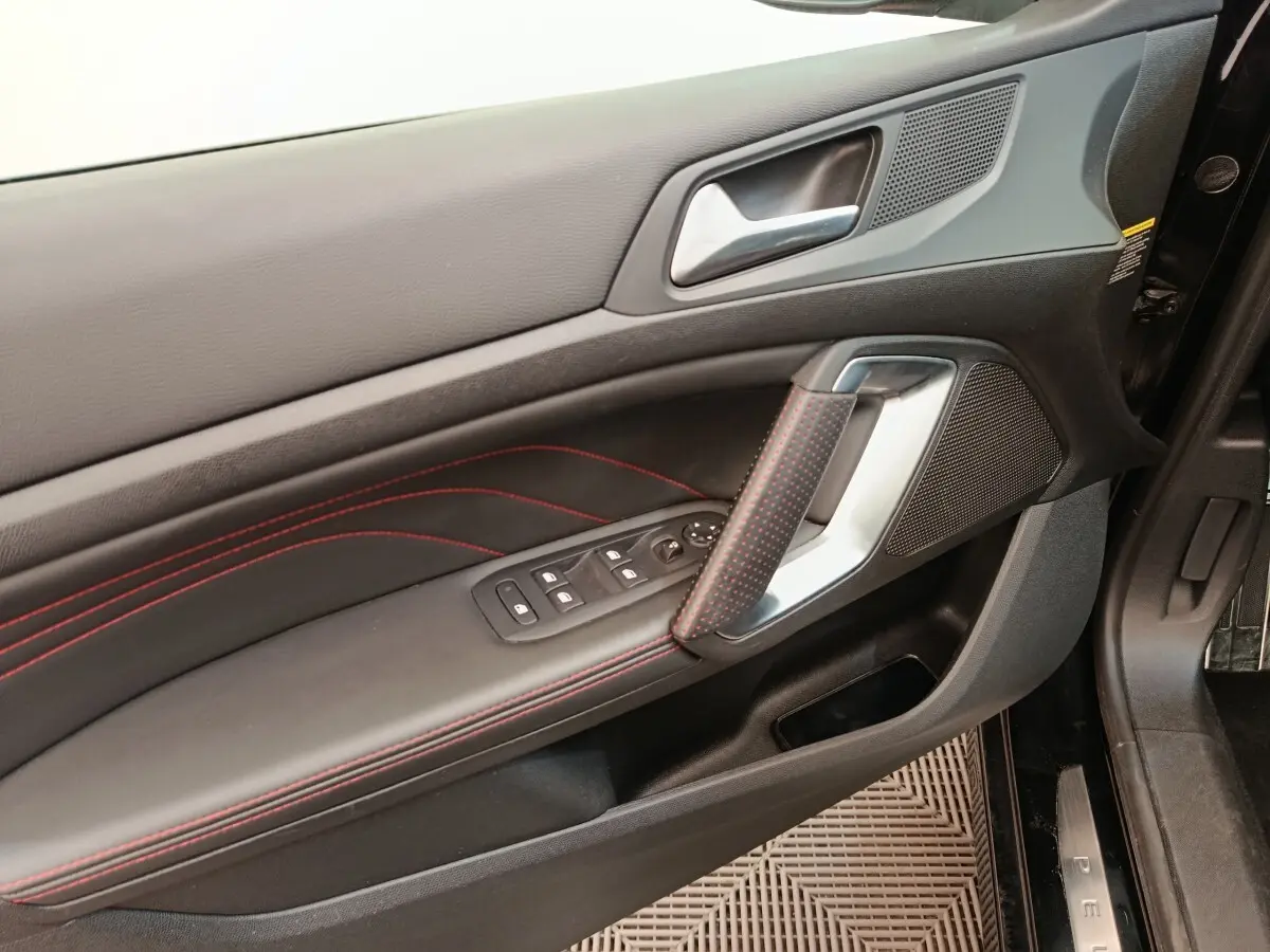 Vue rapprochée de la porte avant gauche noire de la Peugeot 308 GT Line avec surpiqûres rouges et commandes électriques.