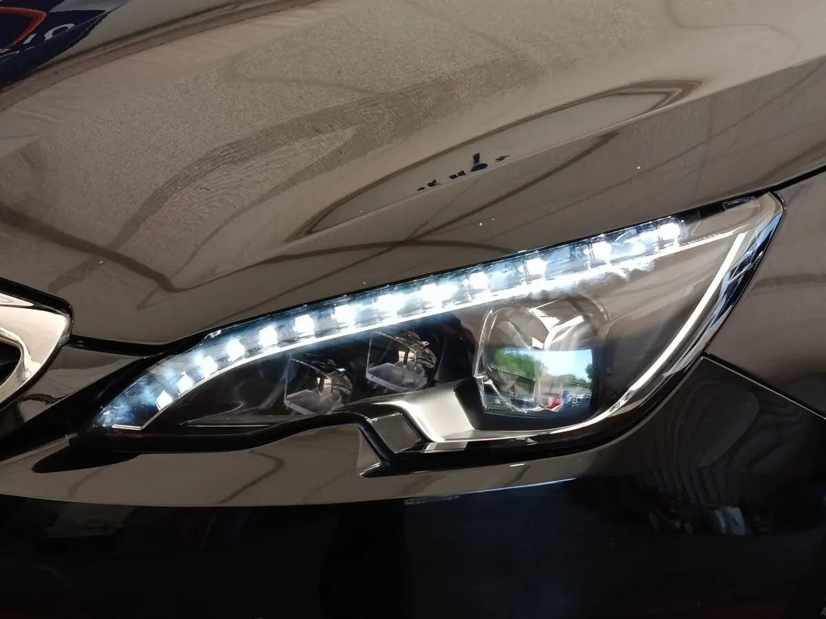 Gros plan sur le phare avant droit LED d'une Peugeot 308 noire, soulignant ses lignes modernes et précises.