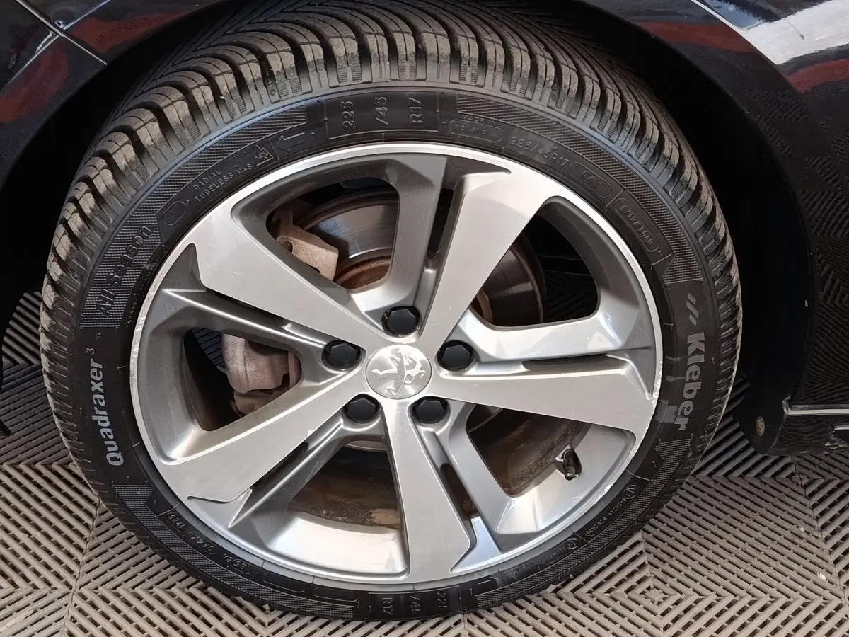 Gros plan sur la roue avant droite d’une Peugeot 308 noire, mettant en valeur la jante alliage et le pneu Kleber.