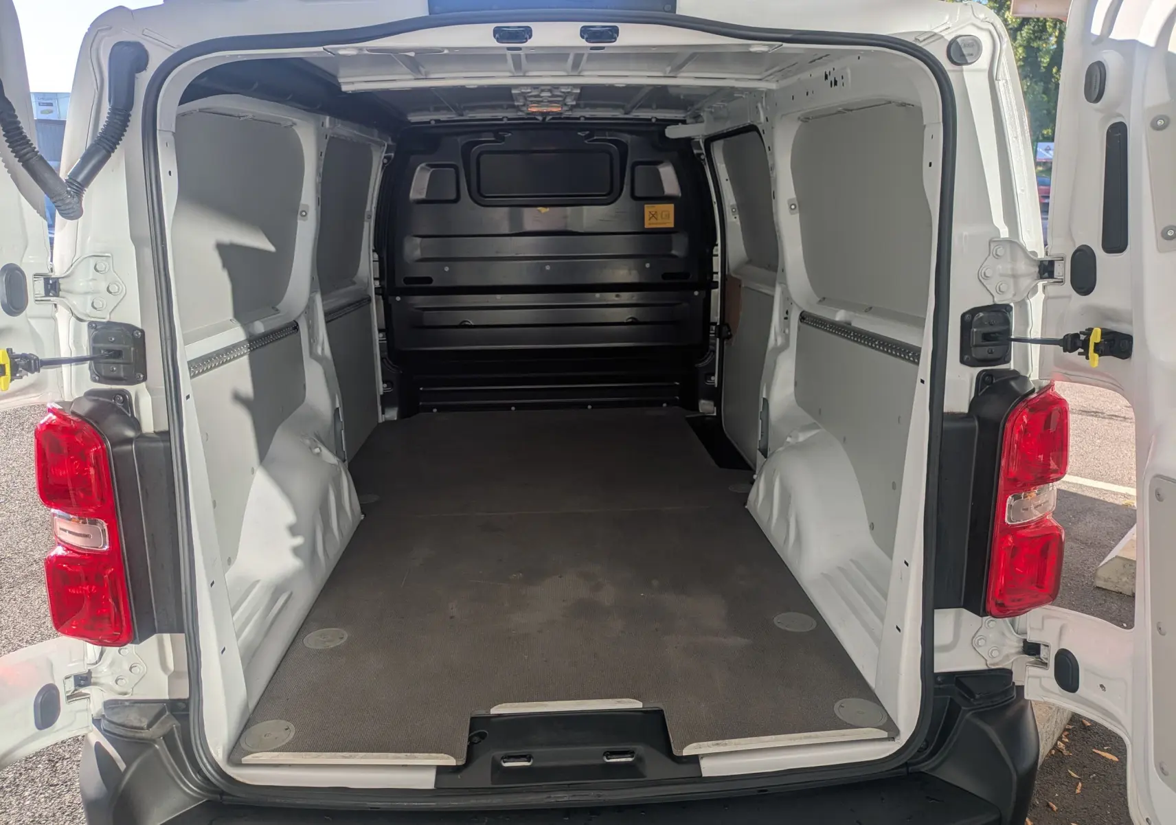 Vue arrière du fourgon blanc FIAT Scudo XL 2025 avec portes ouvertes et espace de chargement vide et modulable.