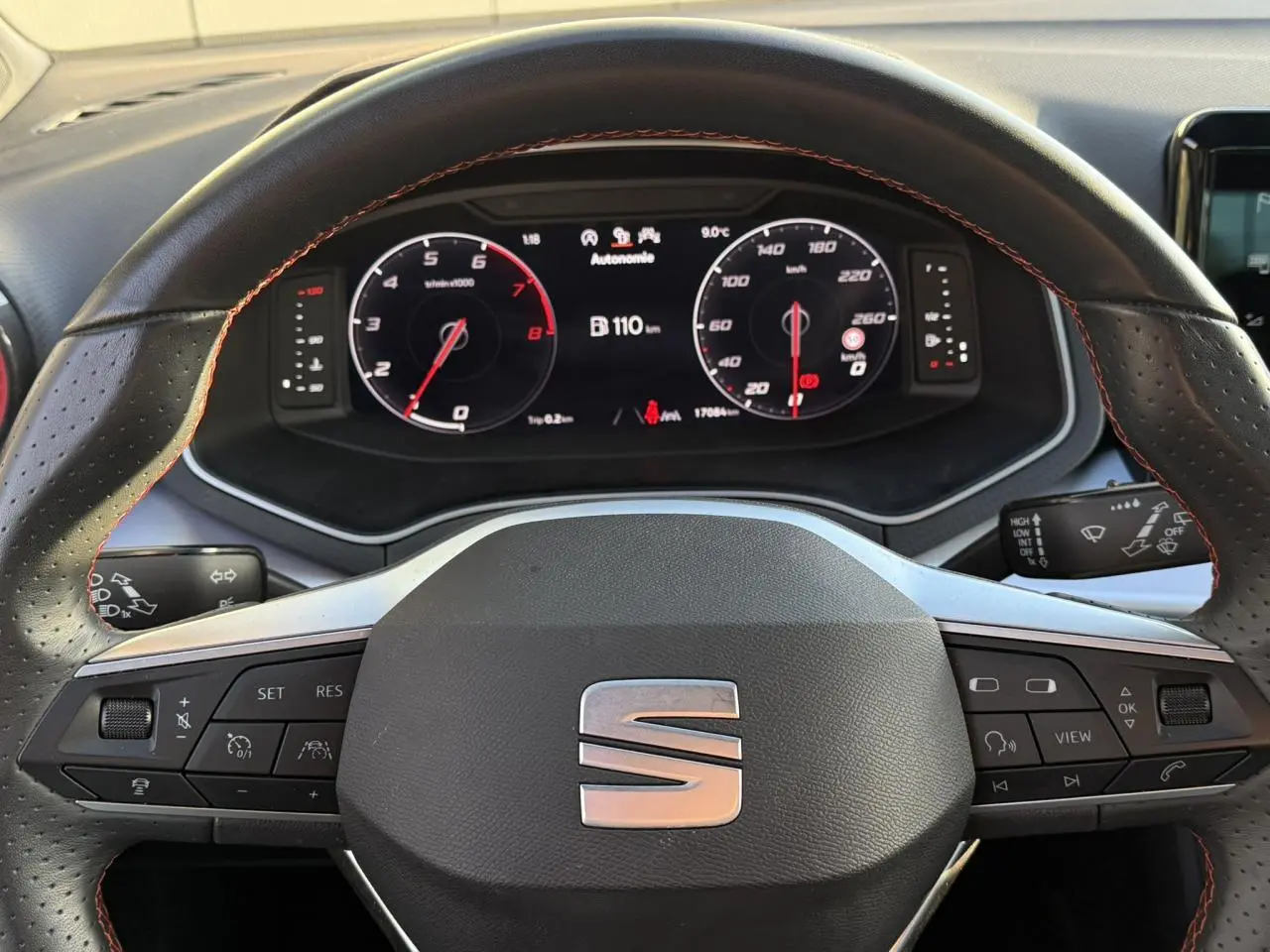 Vue rapprochée du volant en cuir noir avec surpiqûres rouges et tableau de bord digital de la SEAT IBIZA TSI 115 FR.