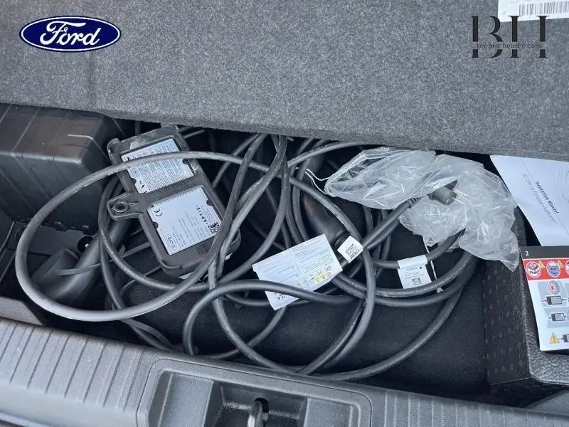 Coffre ouvert montrant un câble de recharge noir enroulé dans un Renault Captur gris Highland et noir Etoile, vue de dessus.