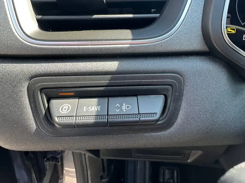 Gros plan sur les boutons de commande E-SAVE et réglage des phares du tableau de bord du Renault Captur gris.