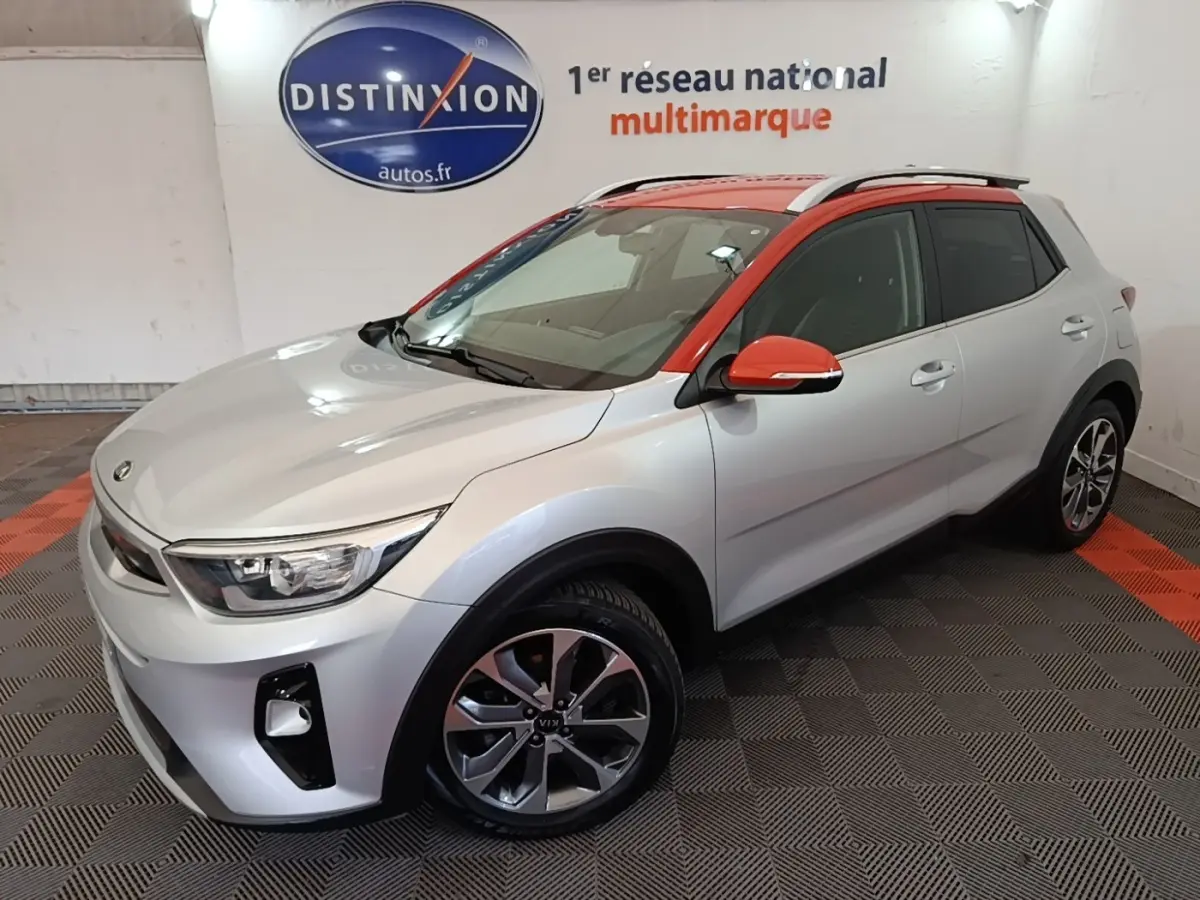 Vue 3/4 avant droit d'un KIA Stonic gris clair avec toit et rétroviseurs orange, roues alliage et barres de toit chromées.