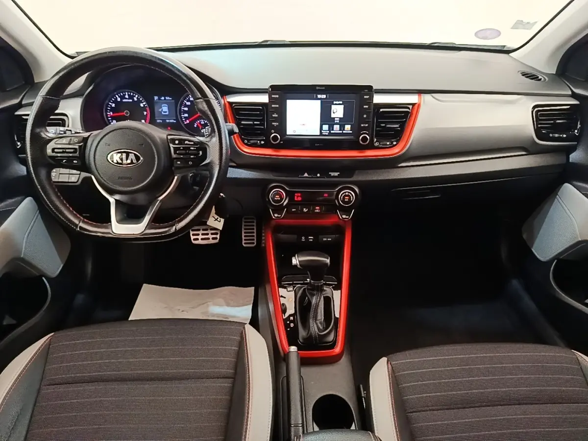 Vue intérieure frontale du tableau de bord et volant KIA Stonic 2019, avec insert rouge autour de l'écran tactile et levier de vitesses.