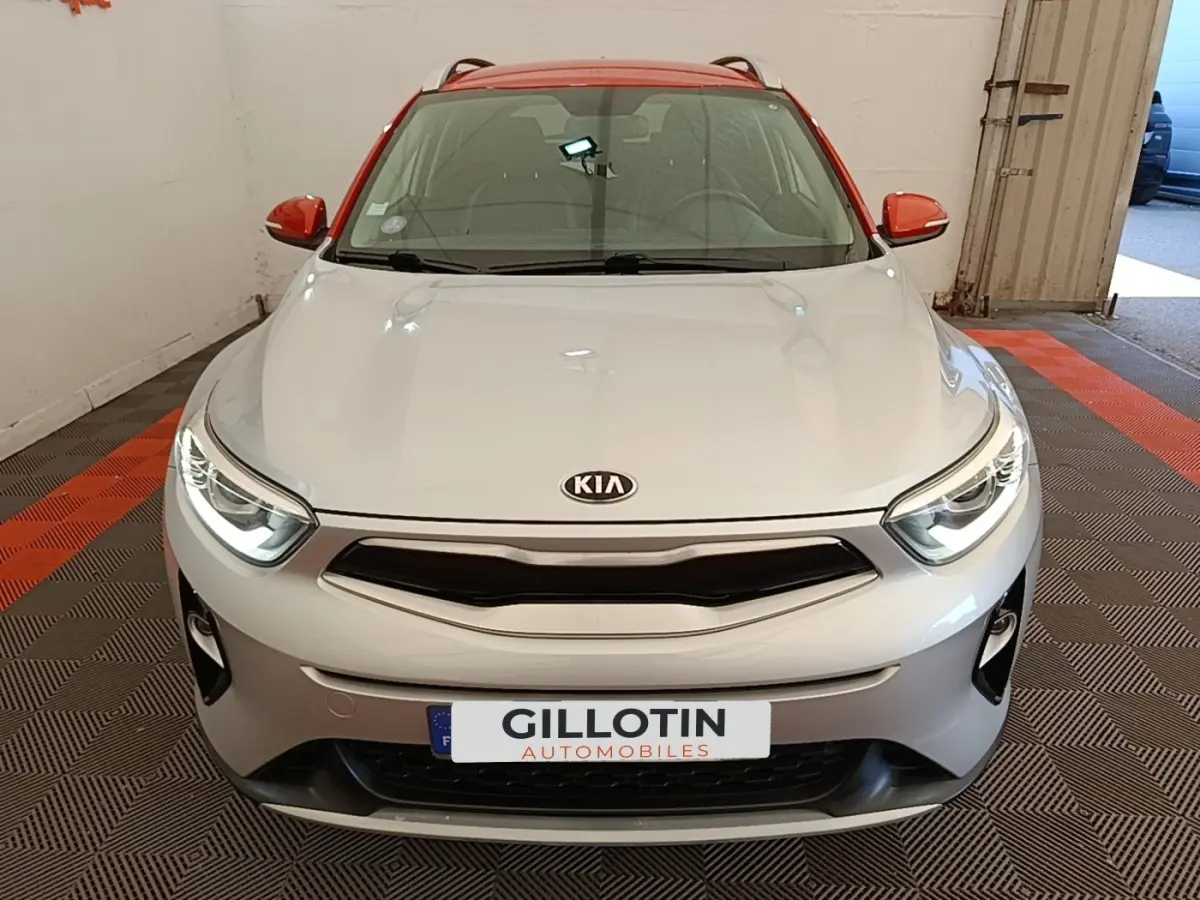Vue avant frontale du KIA Stonic gris clair avec toit et rétroviseurs rouges, phares allumés en intérieur.