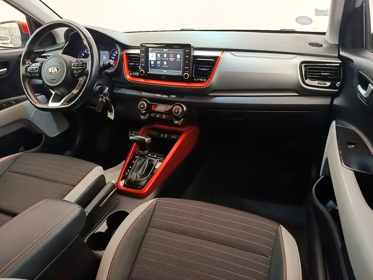 Vue intérieure avant droite du Kia Stonic 2019, tableau de bord gris clair avec inserts orange et écran tactile central.
