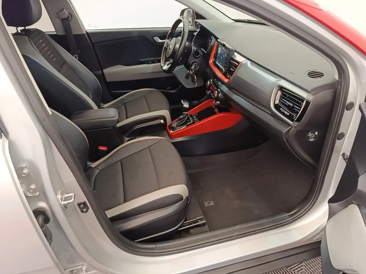 Vue intérieure côté conducteur d'un KIA Stonic gris clair 2019 avec sellerie noire et inserts rouges autour de la console centrale.