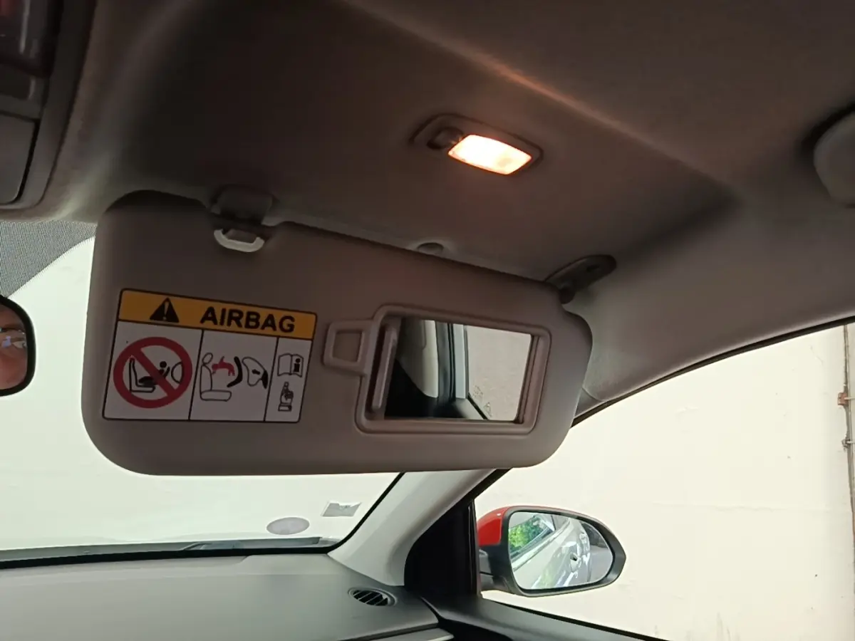 Vue intérieure du pare-soleil côté conducteur avec miroir et lumière, rétroviseur extérieur visible sur fond clair.