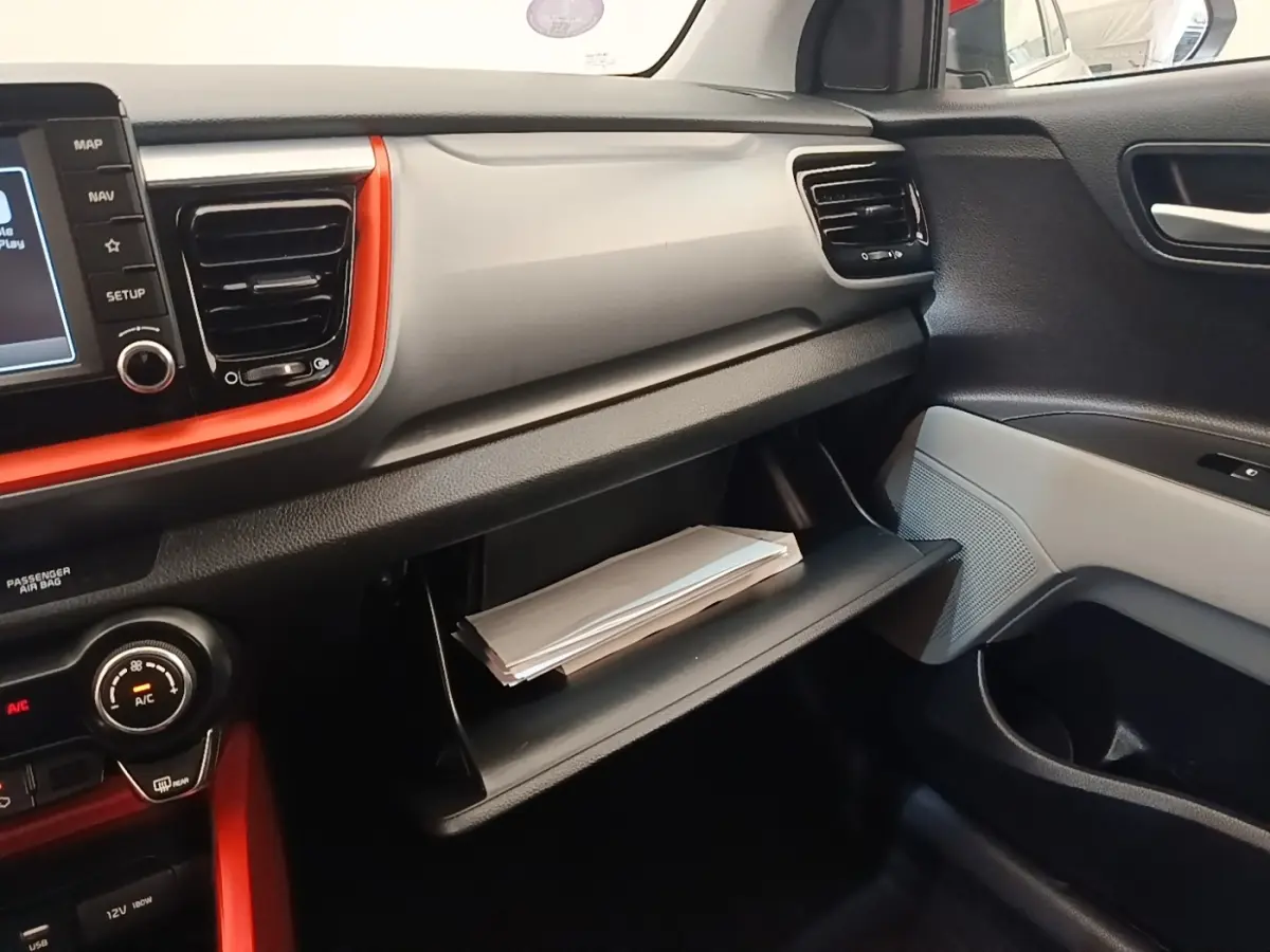 Intérieur KIA Stonic 2019 vu côté passager, tableau de bord gris clair avec encadrement orange et boîte à gants ouverte.
