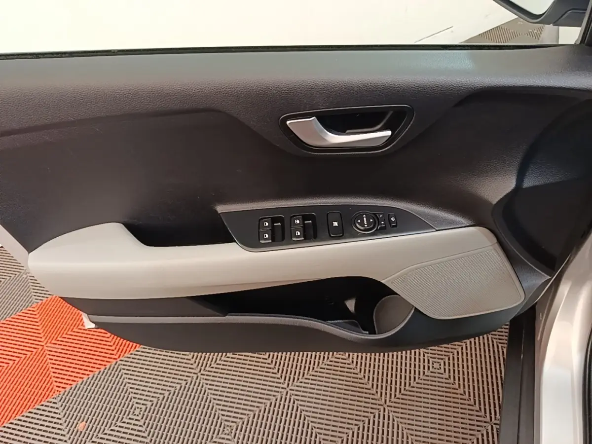 Vue intérieure côté conducteur de la porte d’une KIA Stonic gris clair avec commandes électriques et poignée argentée.