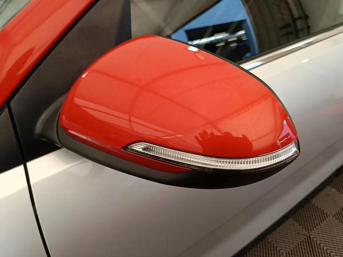 Rétroviseur droit rouge vif avec clignotant intégré sur KIA STONIC gris clair, vue rapprochée côté passager.
