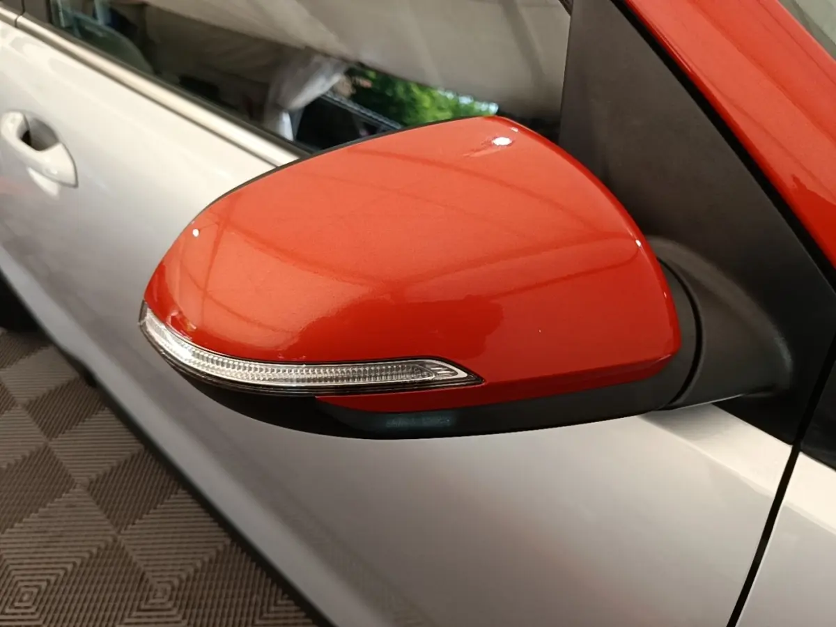 Rétroviseur droit rouge vif avec clignotant intégré sur KIA STONIC gris clair, vue rapprochée côté conducteur.