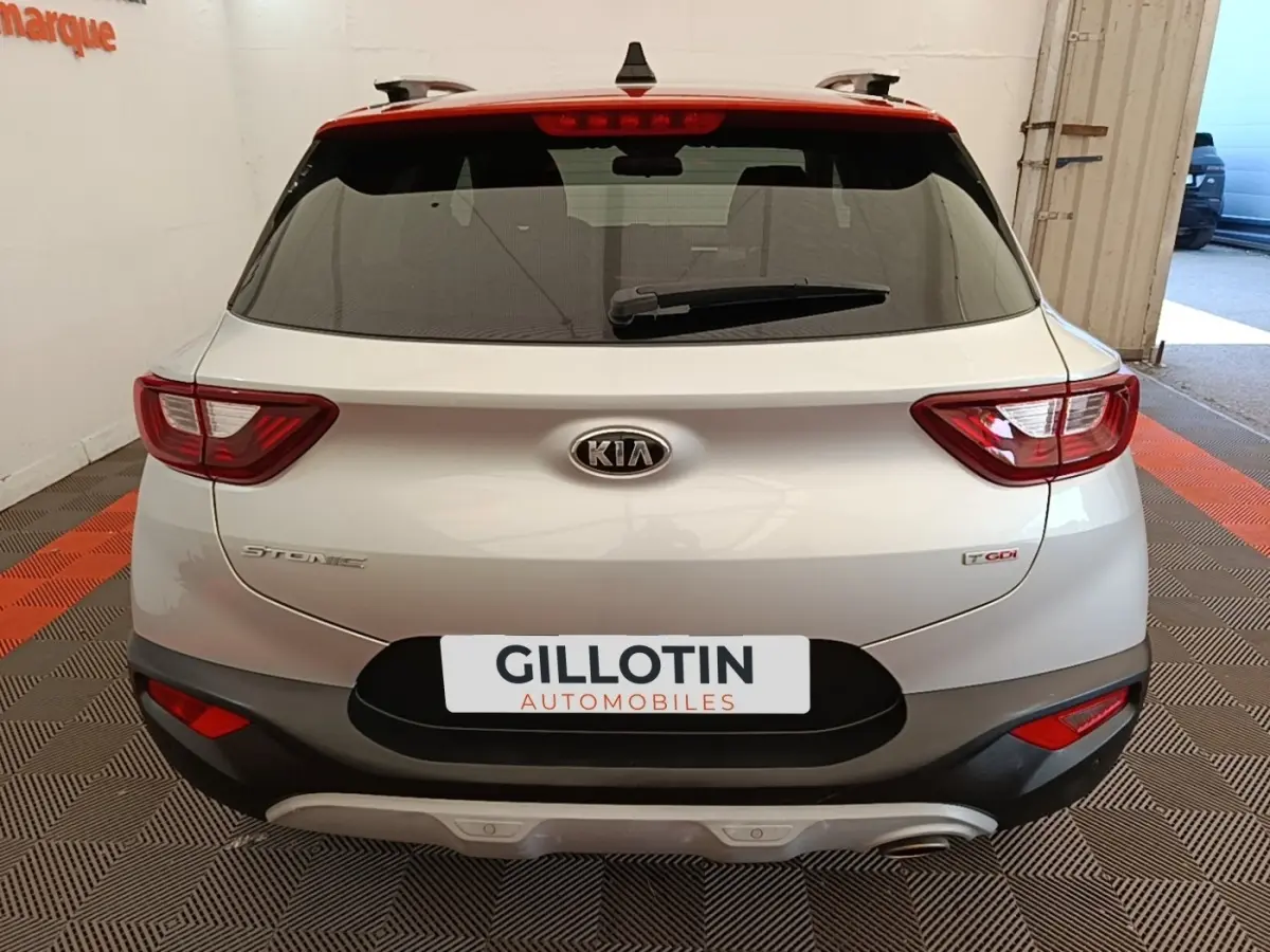 Vue arrière d'un KIA Stonic gris clair avec feux LED et logo visible, stationné en intérieur sur sol à damier.