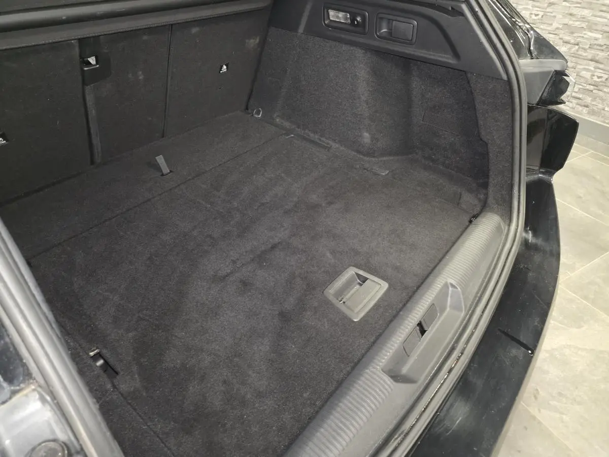 Coffre ouvert vu de l'arrière droit d'une Peugeot 308 SW noire, avec plancher plat et revêtement noir.