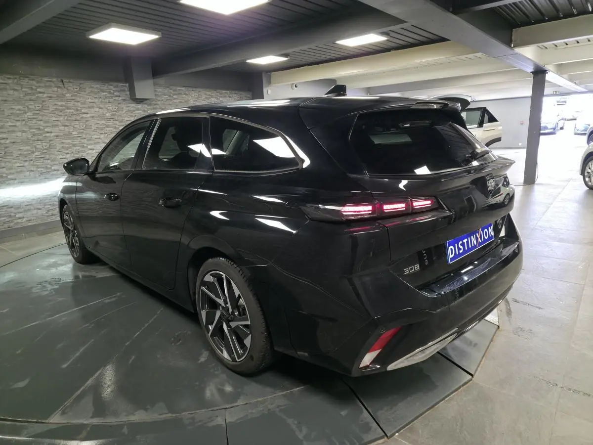 Peugeot 308 SW noire vue 3/4 arrière droit en intérieur, avec feux arrière LED et jantes alliage 17 pouces.