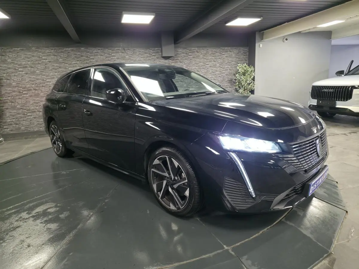 Peugeot 308 SW noire vue en 3/4 avant droit, avec feux LED allumés et jantes alliage 17 pouces.