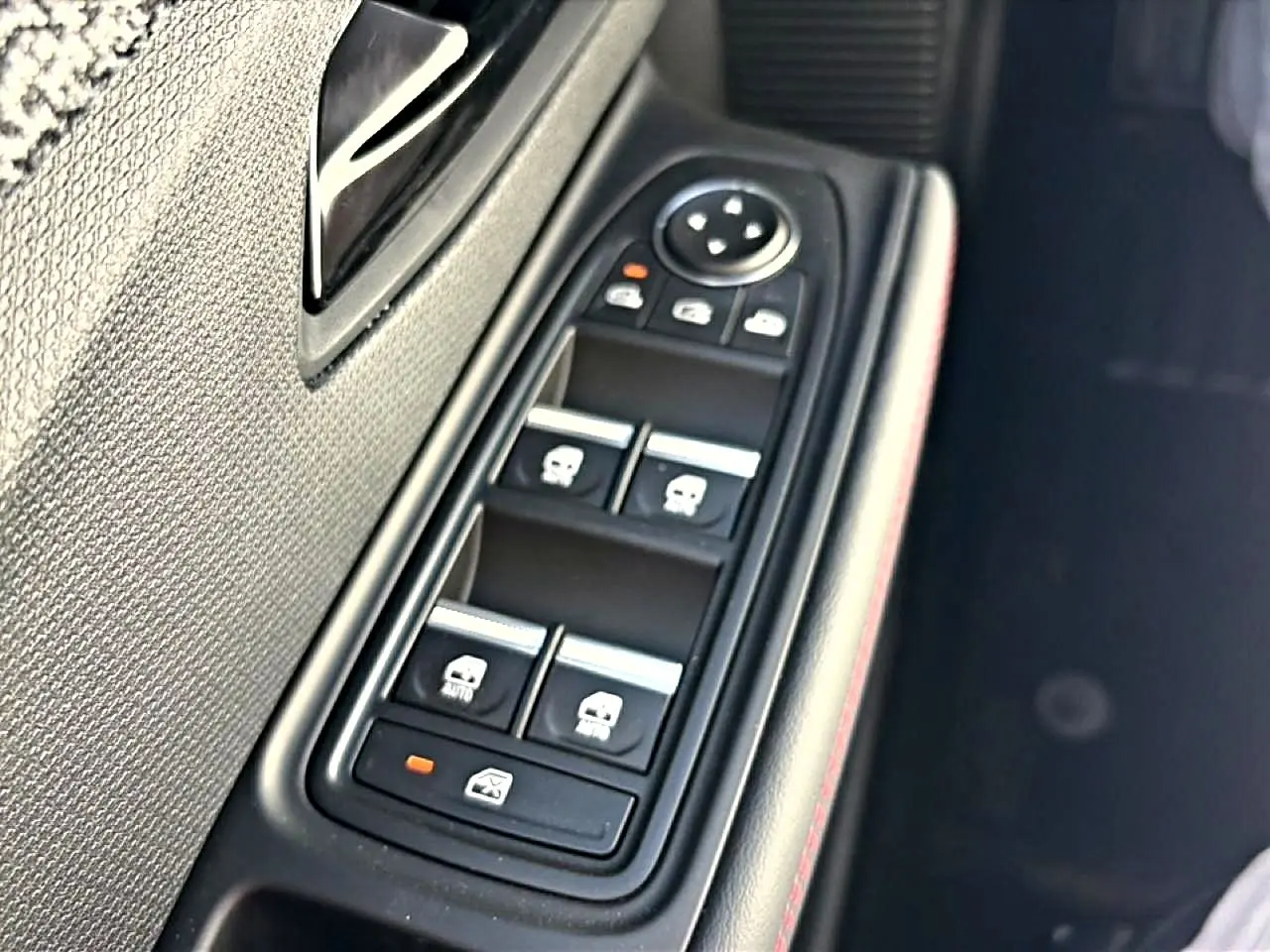 Gros plan sur la commande des vitres électriques côté gauche d’une Renault Clio VI noire, avec surpiqûres rouges.