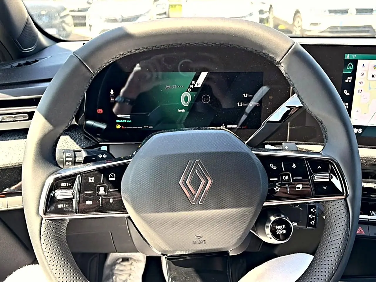 Vue rapprochée du volant noir multifonction de la Renault Clio VI avec tableau de bord numérique en arrière-plan.