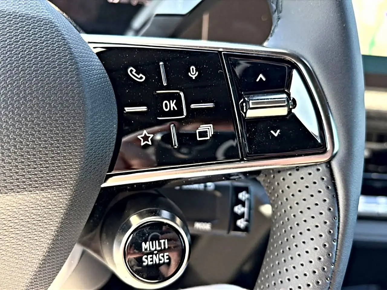 Gros plan sur les commandes multifonctions noires du volant perforé de la Renault Clio VI noire, bouton Multi-Sense visible.