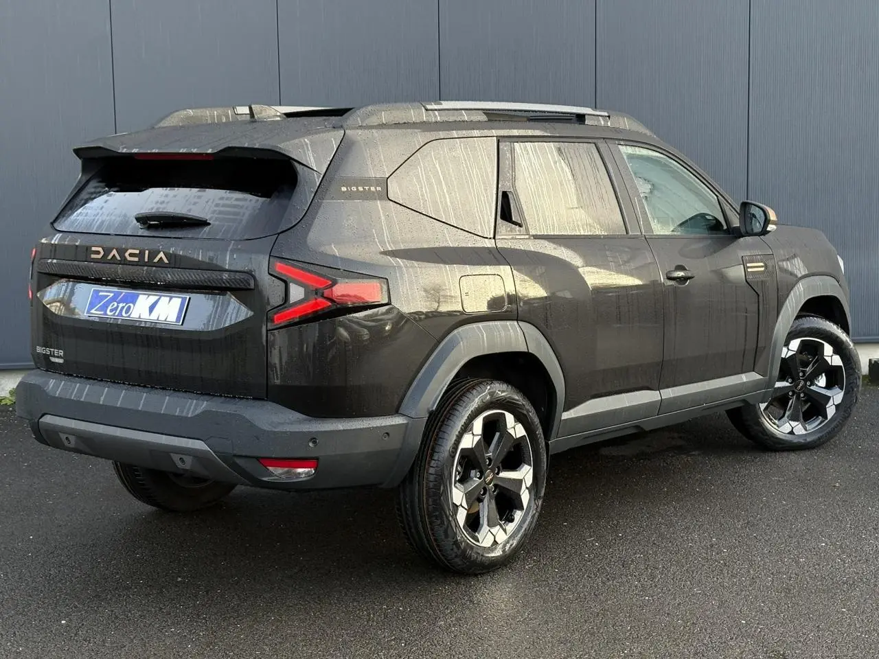 Vue 3/4 arrière droit du Dacia Bigster noir nacré avec jantes alliage 18 pouces et barres de toit modulables.