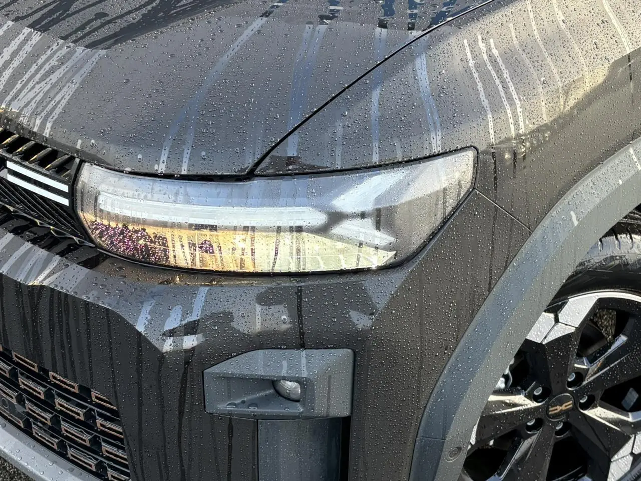 Gros plan sur l'avant droit noir nacré du Dacia Bigster 2025 avec phare allumé et jante alliage diamantée noire.