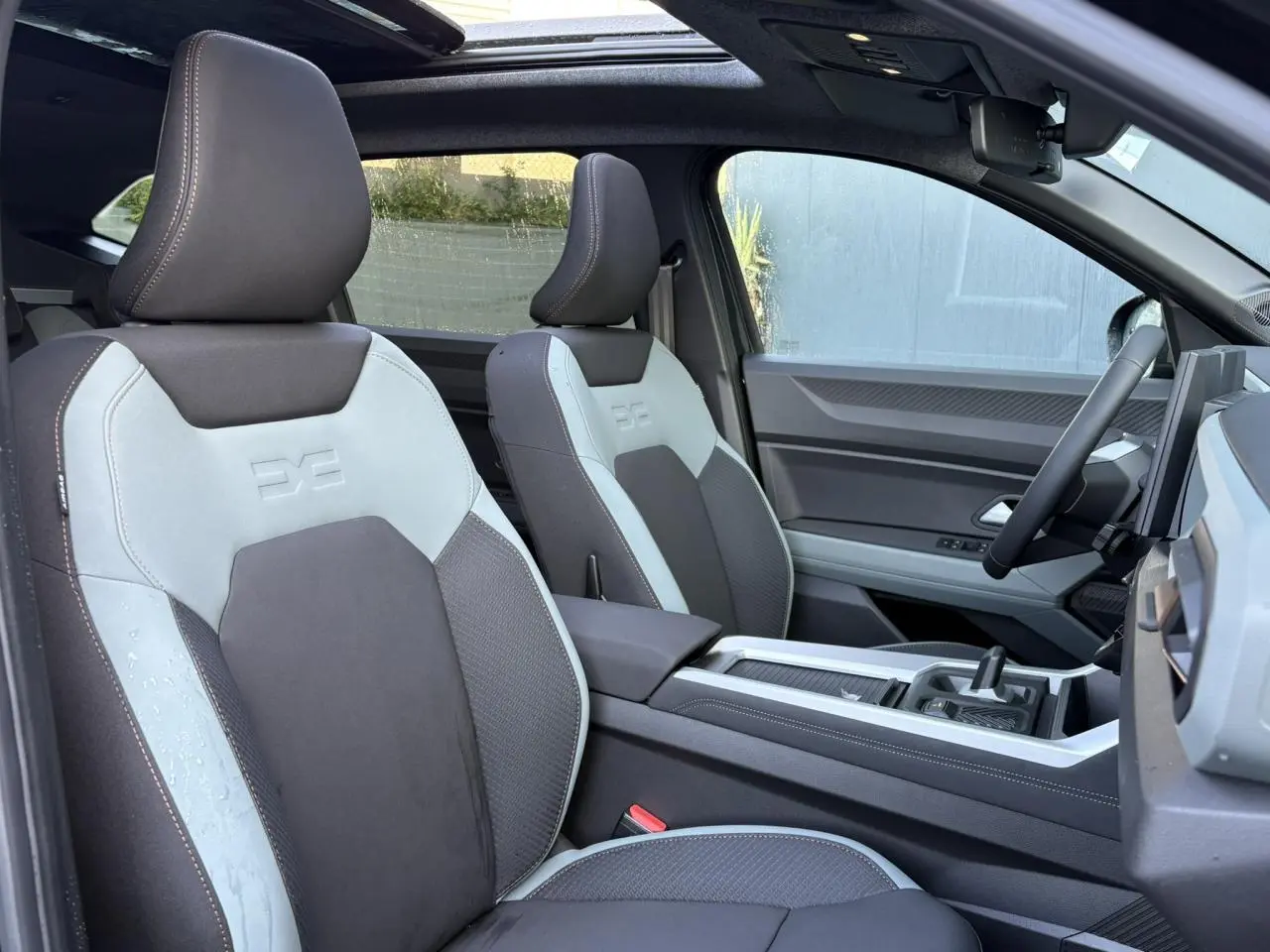 Vue intérieure côté conducteur du Dacia Bigster 2025, sièges Extreme TEP MicroCloud gris clair et foncé avec toit panoramique ouvert.