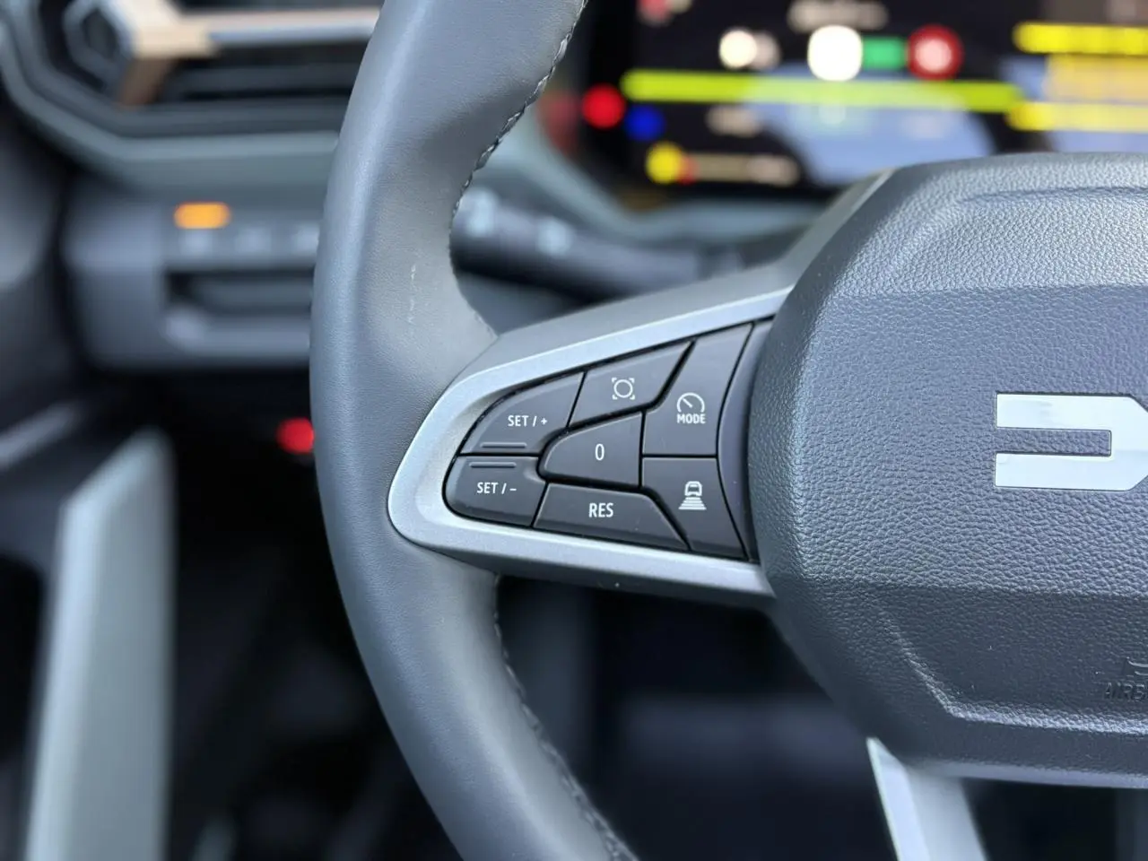 Gros plan sur le volant gris du Dacia Bigster 2025, avec commandes intégrées et logo central partiel visible.