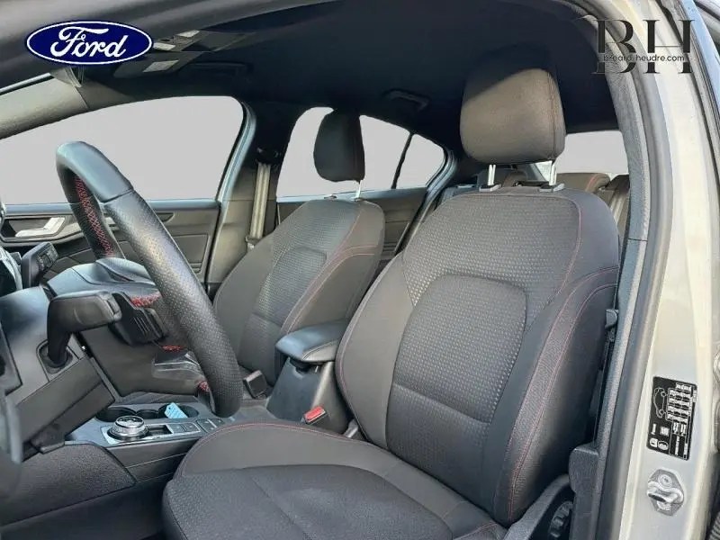 Vue intérieure côté conducteur de la Ford Focus gris lunaire, sièges noirs avec surpiqûres rouges et volant cuir sport.