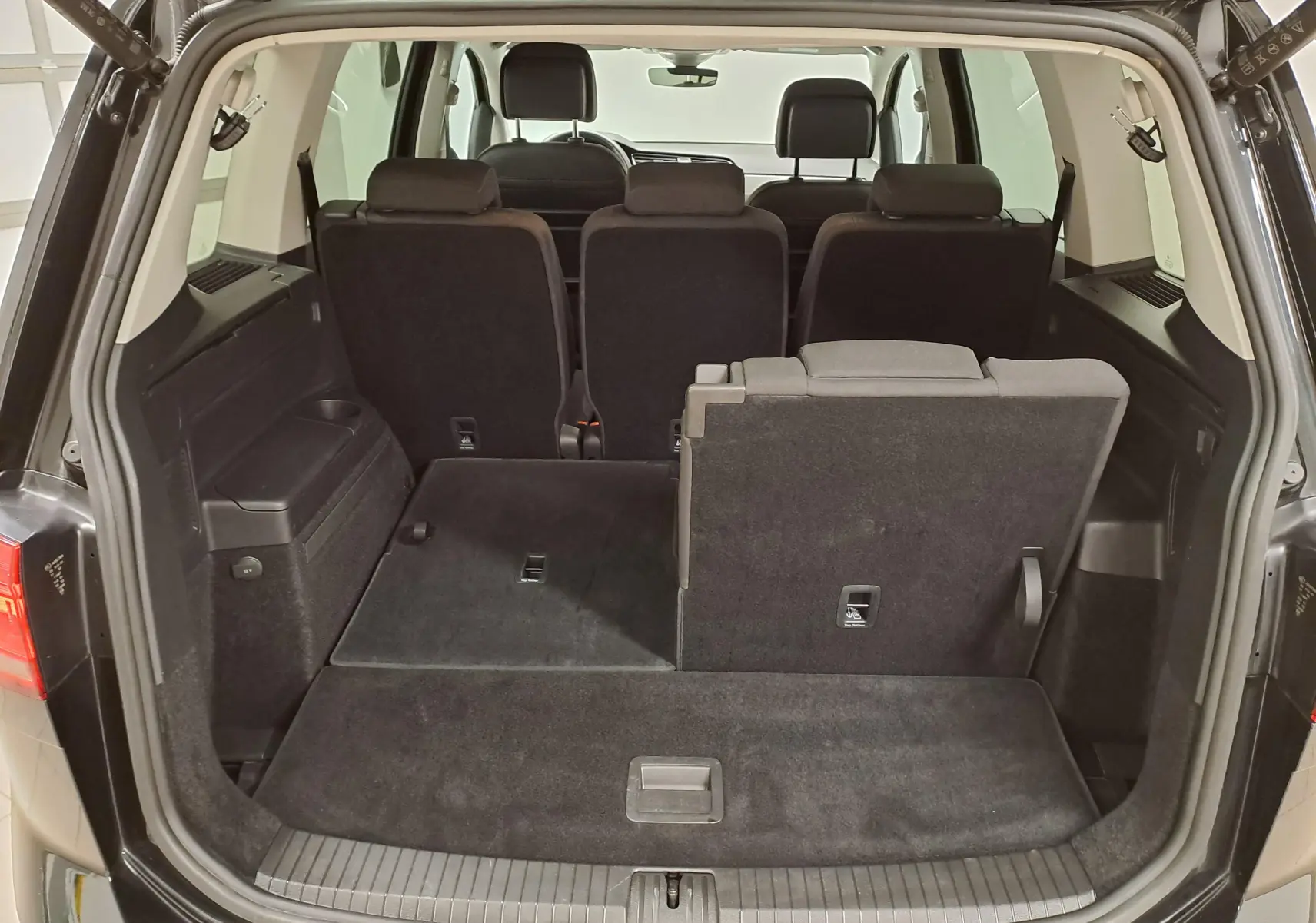 Vue arrière du coffre ouvert du Volkswagen Touran noir intense nacré, montrant les sièges arrière rabattables en partie.