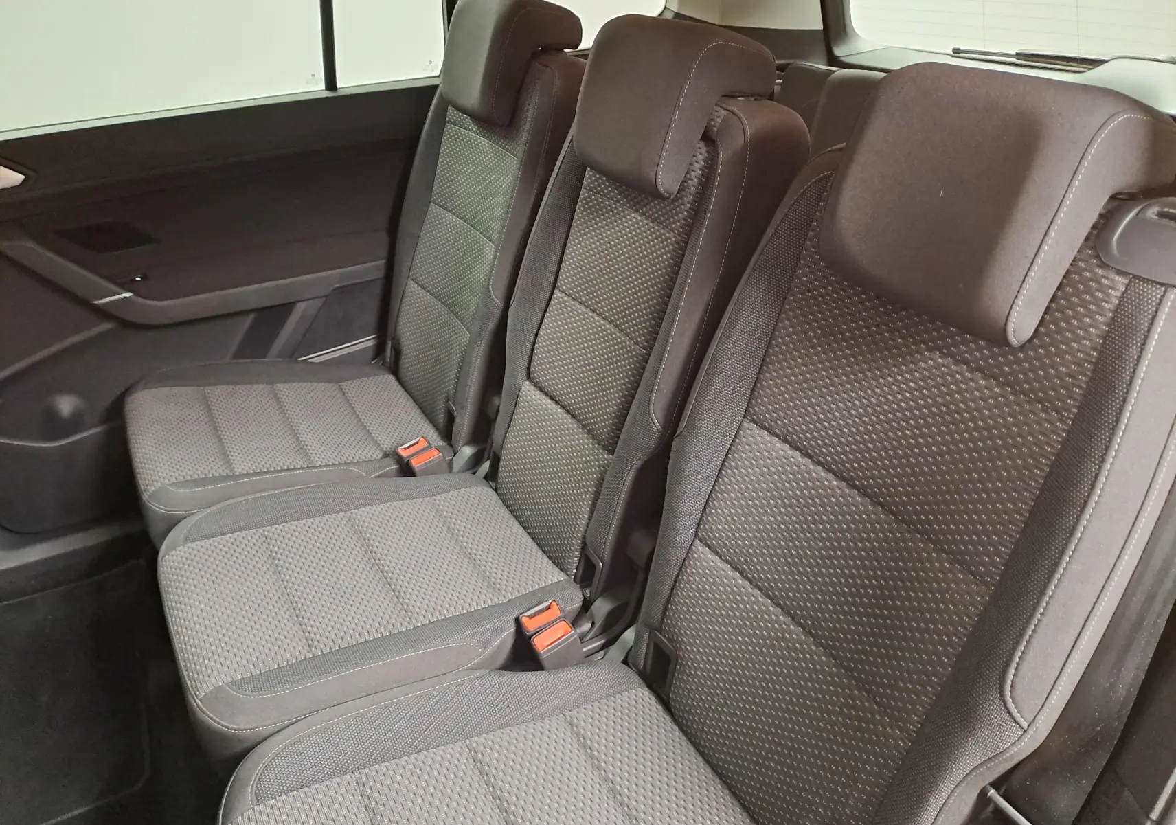 Vue intérieure sur la banquette arrière trois places du Volkswagen Touran 2025, sièges en tissu gris foncé.