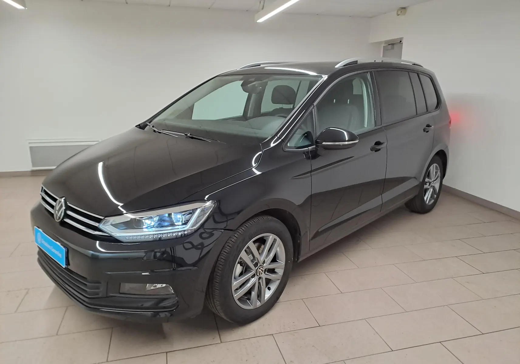 Volkswagen Touran 2025 noir nacré en 3/4 avant droit, avec feux LED et jantes alliage visibles.