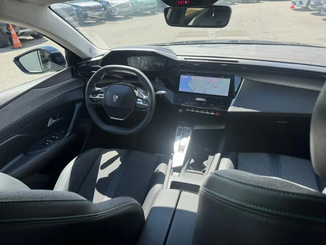 Vue intérieure avant de la Peugeot 308 Hybrid noire 2024, avec volant compact et écran tactile central affichant la navigation.