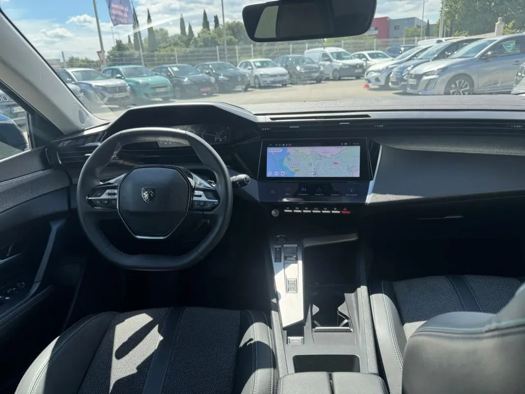 Vue intérieure avant de la Peugeot 308 Hybrid 136 e-DCS6 Allure 2024, tableau de bord avec écran tactile et volant compact noir.