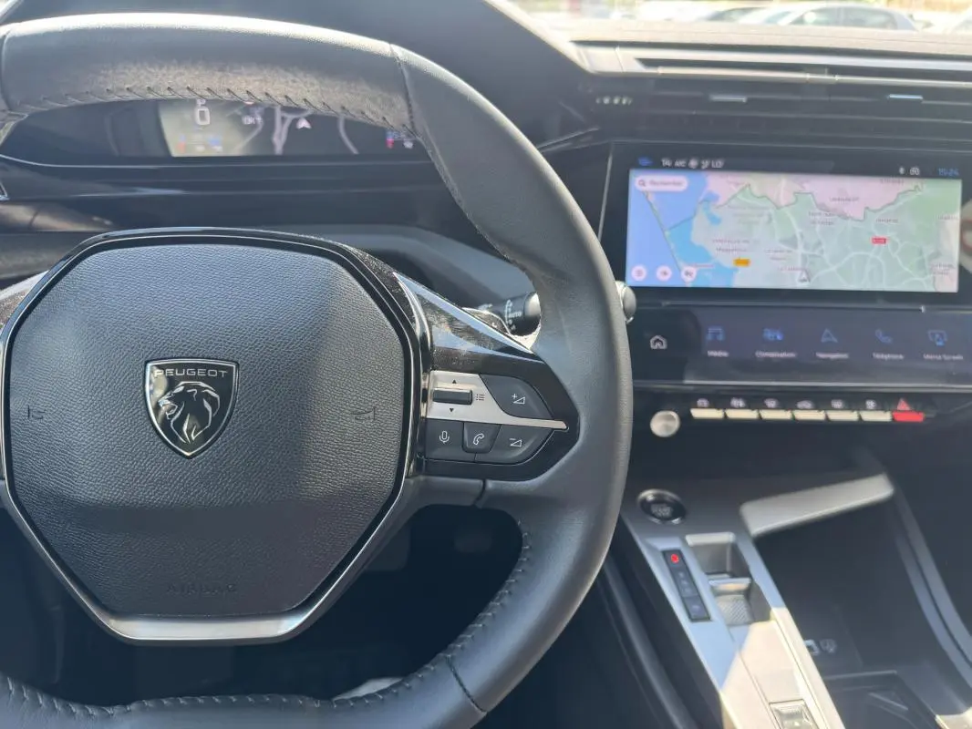 Vue intérieure centrée sur le volant Peugeot noir et le cockpit numérique avec écran tactile affichant une carte de navigation.