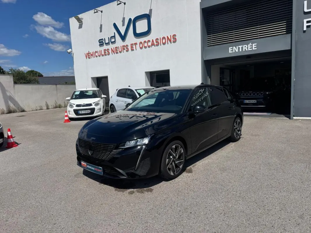 Peugeot 308 Hybrid noir vue 3/4 avant droit, jantes alliage 17 pouces, stationnée devant un concessionnaire.