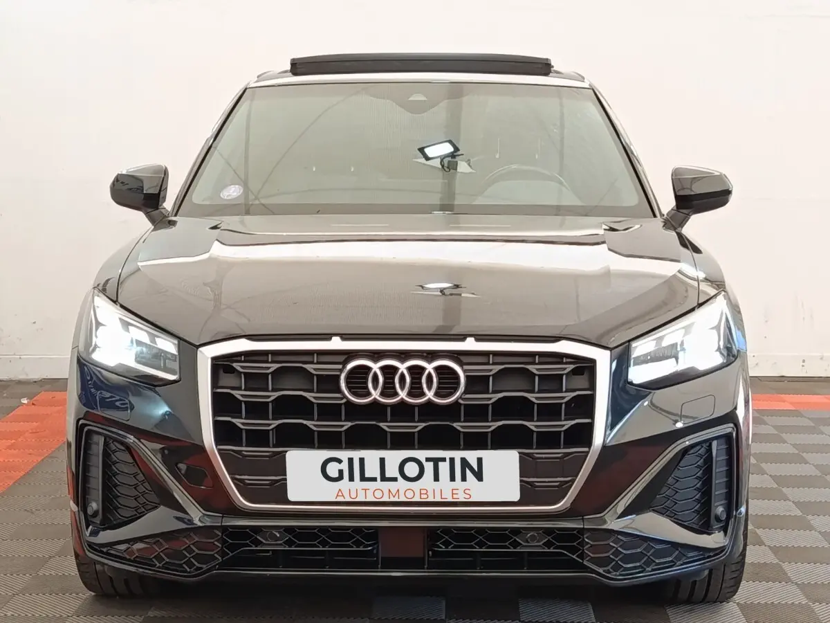 Vue frontale d’un Audi Q2 noir 2021 avec calandre hexagonale et phares LED allumés dans un showroom.