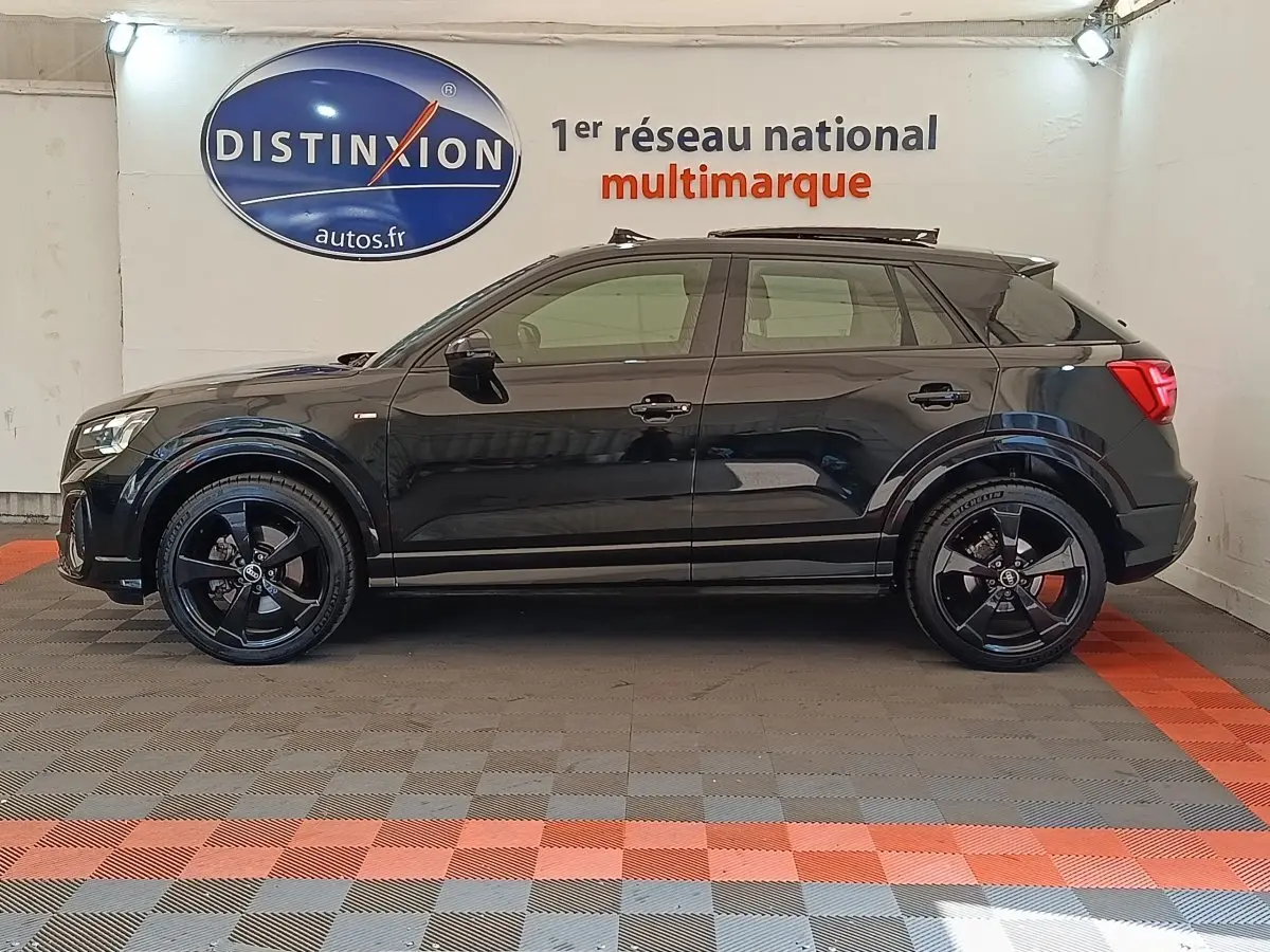 Profil côté gauche d’un Audi Q2 35 TFSI S Line noir 2021, avec jantes noires et toit ouvrant en intérieur showroom.
