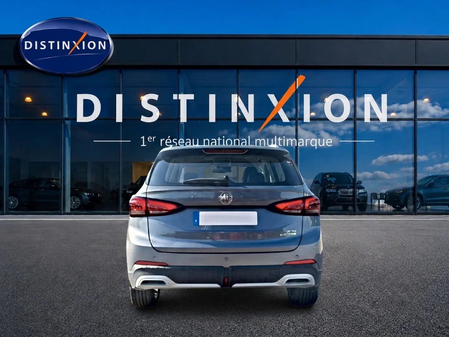 Vue arrière d'un MG Motor ZS gris 1.5 hybrid 197 luxury garé devant une vitrine Distinxion.