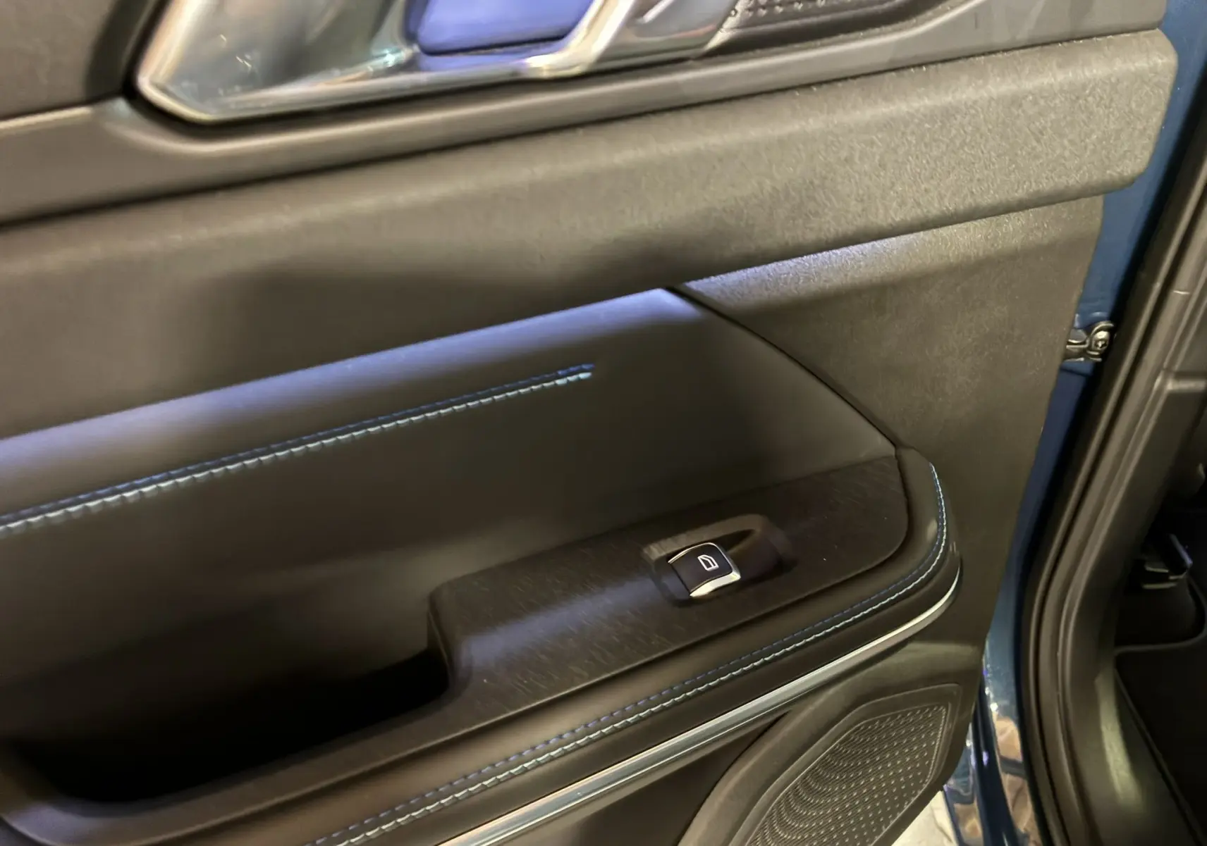 Gros plan sur la porte côté gauche du Lynk & Co 01 bleu 2023, avec surpiqûres bleues et bouton de lève-vitre.